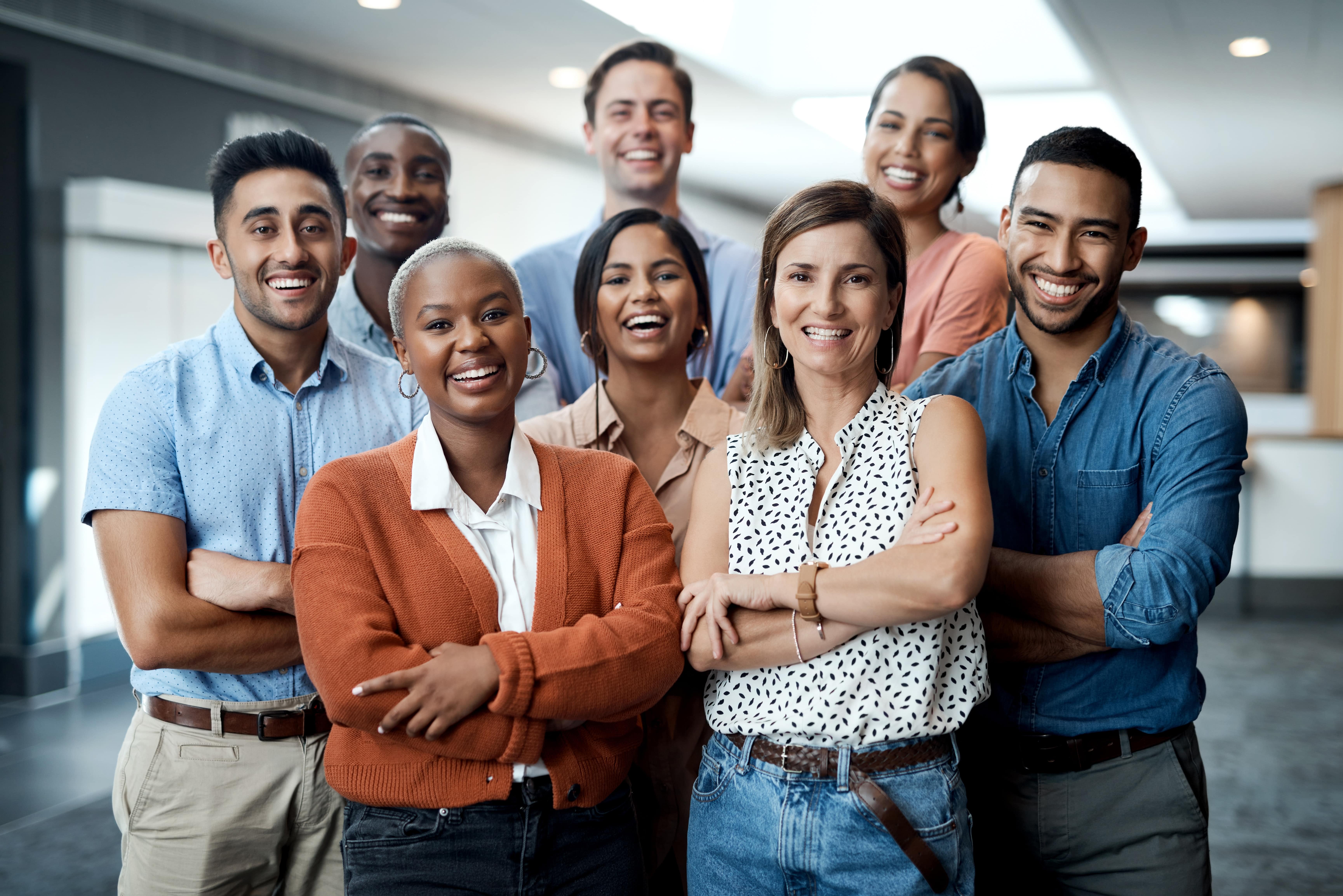 Grupo de oito profissionais sorridentes, de diferentes etnias e idades, em um ambiente corporativo. Eles representam diversidade e inclusão no ambiente de trabalho de uma empresa multinacional. 
