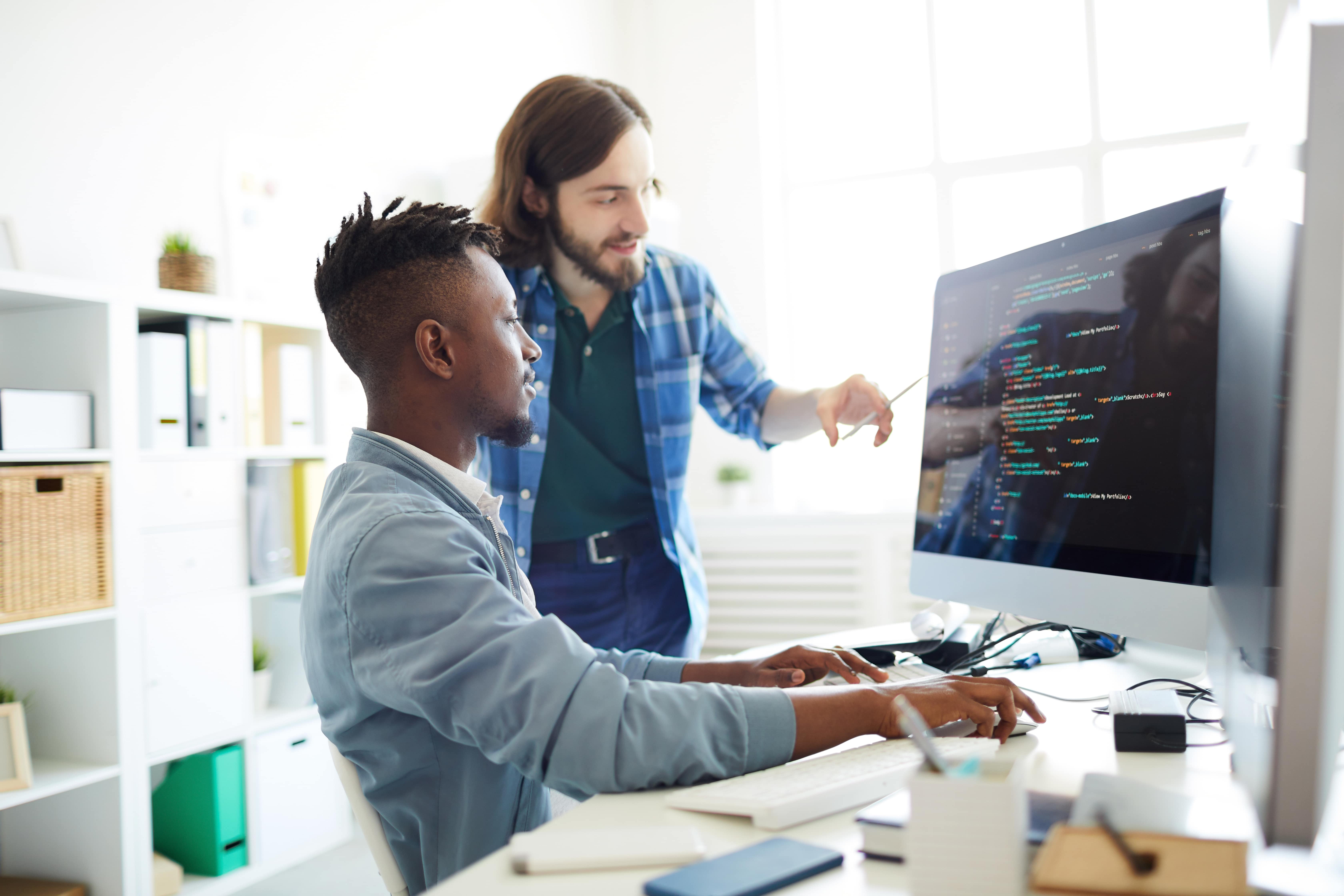 Imagem de dois técnicos de informática trabalhando juntos em um computador com códigos na tela